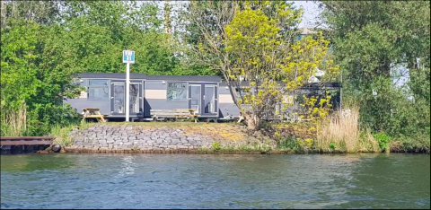 Tiny Wagon tiny house en Marina Parcs Almere, Países Bajos, junto al agua y rodeado de árboles verdes.