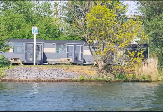 Tiny Wagon tiny house en Marina Parcs Almere, Países Bajos, junto al agua y rodeado de árboles verdes.