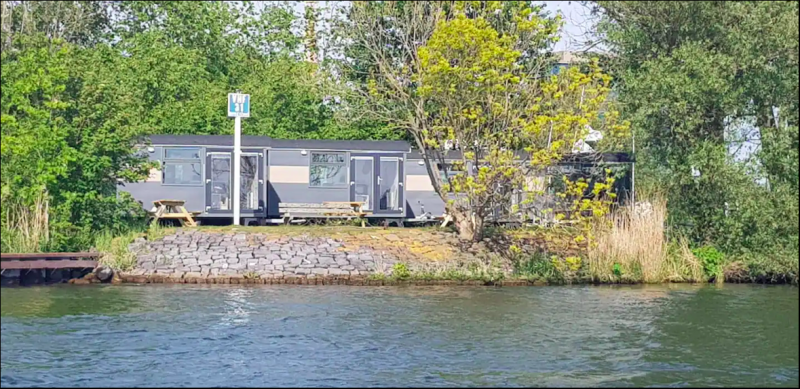 Tiny Wagon tiny house at Marina Parcs Almere in the Netherlands, nestled by the water with trees around.