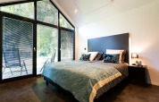 Dormitorio moderno en tiny house con ventanales grandes, cama doble y vista a la naturaleza exterior.