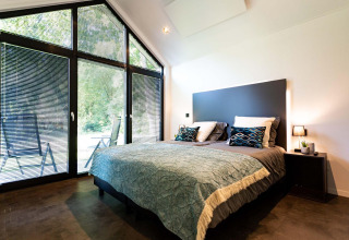 Dormitorio moderno en tiny house con ventanales grandes, cama doble y vista a la naturaleza exterior.