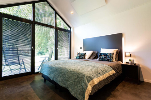 Chambre moderne d’une tiny house avec grandes fenêtres, lit double et vue paisible sur la nature.