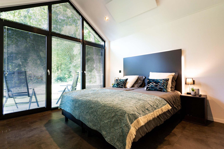 Dormitorio moderno en tiny house con ventanales grandes, cama doble y vista a la naturaleza exterior.