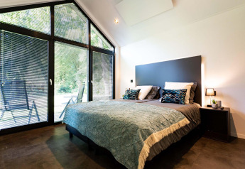 Dormitorio moderno en tiny house con ventanales grandes, cama doble y vista a la naturaleza exterior.