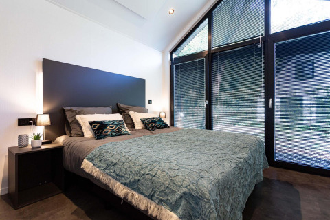 Modern slaapkamerinterieur in een tiny house met grote ramen, jaloezieën en een strak opgemaakt bed.
