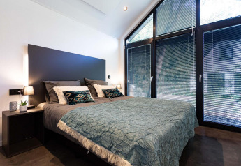 Camera da letto moderna in una tiny house con grandi finestre, tende alla veneziana e arredo minimalista.