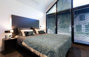 Modernes Schlafzimmer in einem Tiny House mit großen Fenstern, Jalousien und stilvollem, minimalistischem Dekor.
