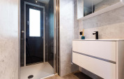 Salle de bain moderne d'une tiny house avec douche vitrée, grande fenêtre, lavabo suspendu et murs en marbre.