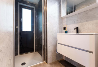 Baño moderno en una tiny house con ducha de cristal, ventana grande, lavabo flotante y paredes de mármol.