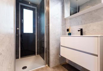 Modern bathroom in a tiny house featuring a glass shower, large window, floating sink and marble walls.
