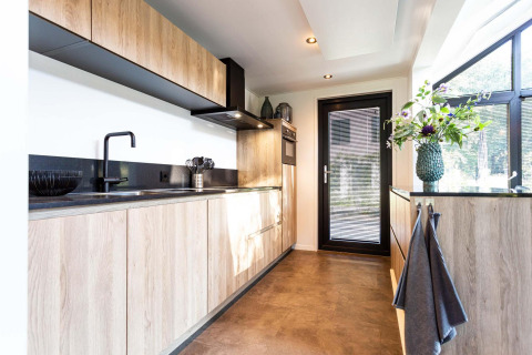 Modern tiny house kitchen with wood cabinets, black fixtures, and a large window letting in natural light.