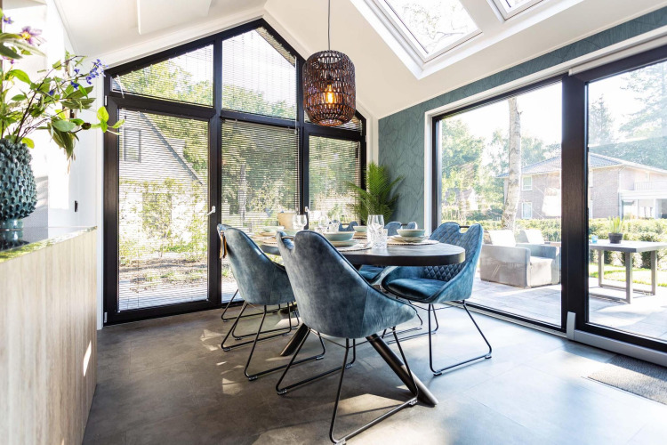 Luminoso comedor moderno en una tiny house con grandes ventanales, sillas azules y vistas al jardín.