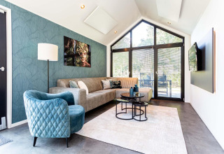 Moderne tiny house living met grote ramen, blauwe stoel, gezellige zetel en stijlvol wanddecor.