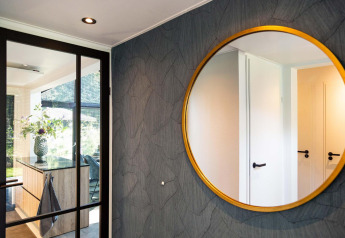 Interno di tiny house moderno con grande specchio tondo, porta in vetro e cucina luminosa con fiori.