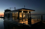 Hausboot ‚Earrebarre‘ bei Welcome In - Friesland, Niederlande, am Abend mit warmem Licht im Inneren.
