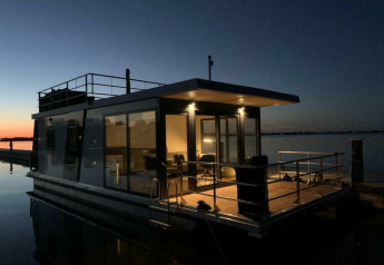 Hausboot ‚Earrebarre‘ bei Welcome In - Friesland, Niederlande, am Abend mit warmem Licht im Inneren.