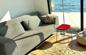 Sunny living room with a sofa, red triangular table, and waterfront view from Houseboat 'Earrebarre' in Friesland, Netherlands.