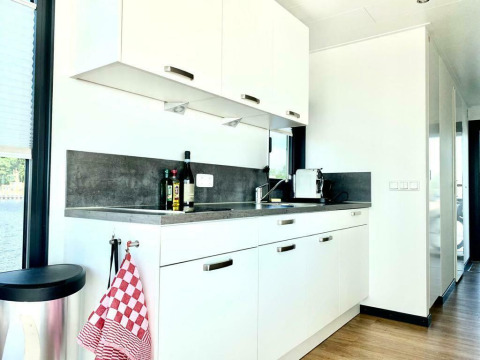 Cuisine moderne de la péniche 'Earrebarre' avec placards blancs et lumière naturelle à Friesland, Pays-Bas.