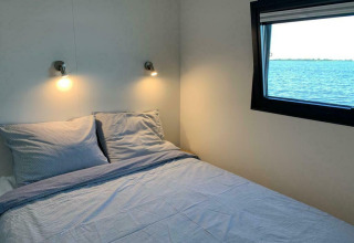 Dormitorio con cama doble, apliques de pared y ventana con vistas al lago en una casa flotante en Friesland.