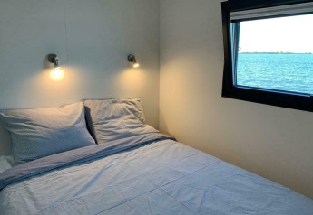 Camera da letto con letto matrimoniale, luci a parete e finestra con vista lago su una houseboat in Friesland.