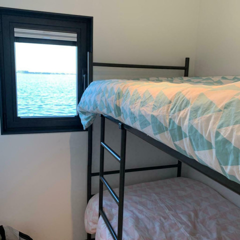 Zimmer mit Etagenbetten und Blick auf das Wasser durch ein Fenster auf dem Hausboot 'Earrebarre' in Friesland, Niederlande.