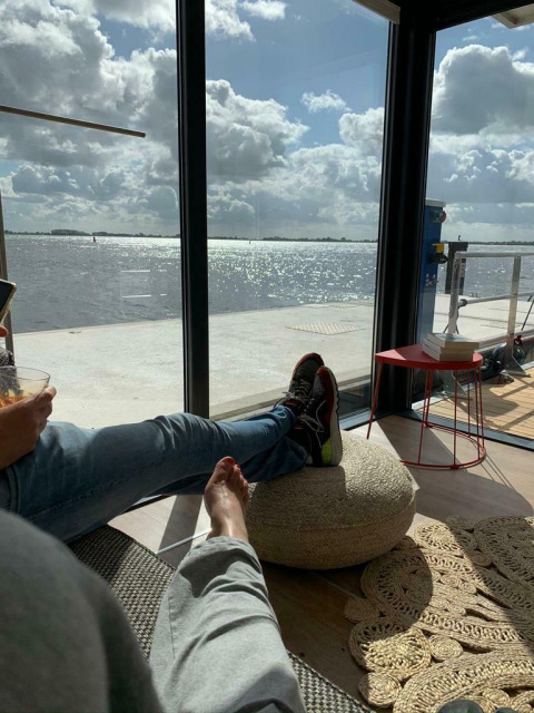 Vista relajada desde la casa flotante 'Earrebarre' con los pies arriba, lago y nubes en Friesland, Países Bajos.