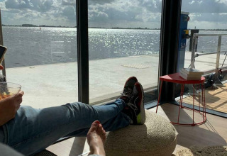 Vista relajada desde la casa flotante 'Earrebarre' con los pies arriba, lago y nubes en Friesland, Países Bajos.