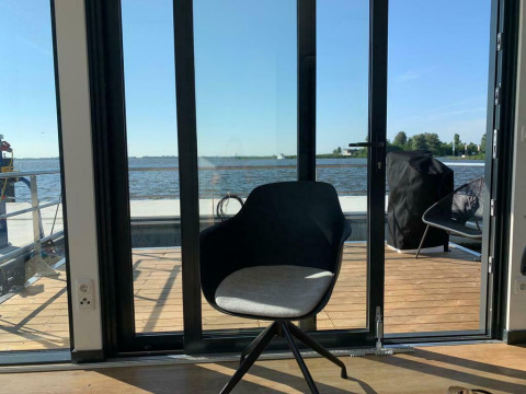 Moderner Stuhl an Glastüren mit Blick aufs Wasser auf dem Hausboot 'Earrebarre' in Friesland, Niederlande.