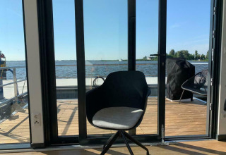 Chaise moderne devant des portes vitrées avec vue sur l’eau à bord de la péniche 'Earrebarre' en Frise, Pays-Bas.