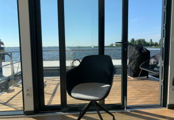 Moderner Stuhl an Glastüren mit Blick aufs Wasser auf dem Hausboot 'Earrebarre' in Friesland, Niederlande.