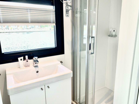 Salle de bain lumineuse sur la péniche 'Earrebarre' avec lavabo, fenêtre et douche à Friesland, Pays-Bas.