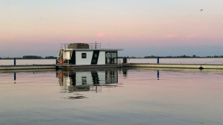 Houseboat 'Earrebarre' flottant sur l’eau calme au coucher du soleil à Friesland, Pays-Bas, avec reflets paisibles.