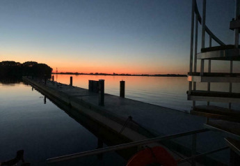 Sonnenuntergang über ruhigem Wasser mit Steg, aufgenommen vom Hausboot Earrebarre in Friesland, Niederlande.