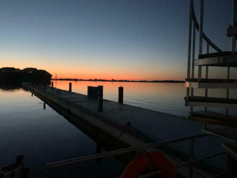 Atardecer sobre aguas tranquilas con muelle, visto desde la casa flotante Earrebarre en Friesland, Países Bajos.