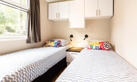 Deux lits simples avec des coussins colorés dans une chambre lumineuse de la Silva Wellness Lodge à Landgoed de Scheleberg.
