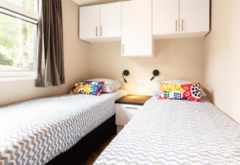 Twee eenpersoonsbedden met kleurrijke kussens in een lichte kamer bij Silva Wellness Lodge op Landgoed de Scheleberg.