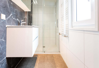 Moderne badeværelse med ophængt vask, regnbruser og stor vindue på Silva Wellness, Landgoed de Scheleberg.