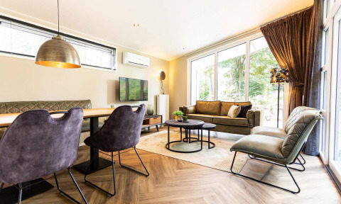 Sala moderna en Silva Wellness Lodge, Landgoed de Scheleberg, Países Bajos, con grandes ventanales y decoración elegante.