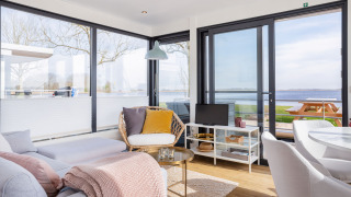 Soleado interior moderno de casa flotante con grandes ventanales, vista al agua y zona de estar en Friesland.