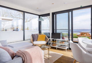 Soleado interior moderno de casa flotante con grandes ventanales, vista al agua y zona de estar en Friesland.