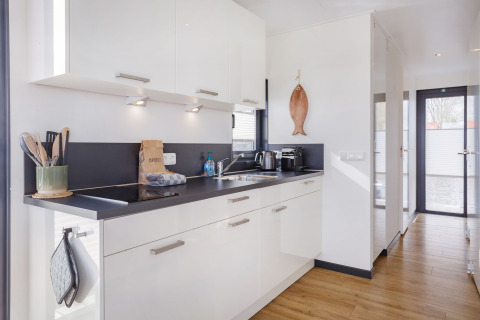 Cocina moderna en la casa flotante Aqua Dolce en Friesland, Países Bajos, con gabinetes blancos y suelo de madera.