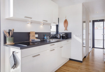 Cocina moderna en la casa flotante Aqua Dolce en Friesland, Países Bajos, con gabinetes blancos y suelo de madera.