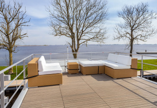 Area lounge esterna su una houseboat a Friesland, Paesi Bassi, con vista sul lago e alberi spogli.