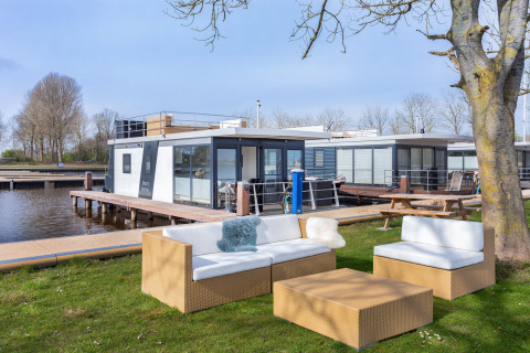 Lounge zithoek op grasveld naast een moderne woonboot en steiger in Friesland, Nederland, bij water.