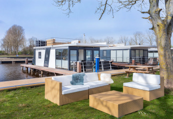 Outdoor lawn seating with wicker furniture by a modern houseboat and dock in Friesland, Netherlands.