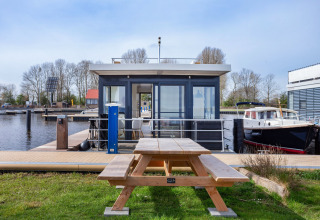 Woonboot Aqua Dolce bij Welcome In - Friesland, Nederland, met picknicktafel en zicht op de haven.