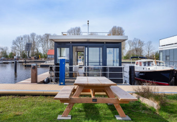 Husbåd Aqua Dolce ved Welcome In - Friesland i Holland, med en bænk og udsigt til havnen.