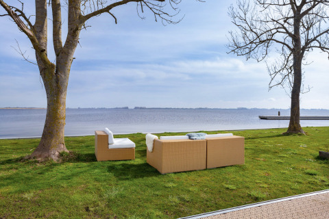 Divani moderni all’aperto su prato verde vicino al lago presso Houseboat Aqua Dolce, Friesland, Paesi Bassi.