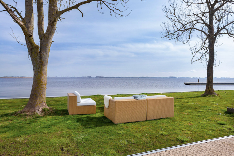 Outdoor seating area with modern sofas on green grass by the lake at Houseboat Aqua Dolce in Friesland, Netherlands.