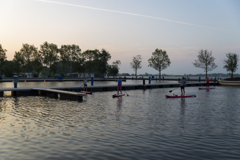 Personas haciendo paddle surf al atardecer cerca de la casa flotante Aqua Dolce en Friesland, Países Bajos.